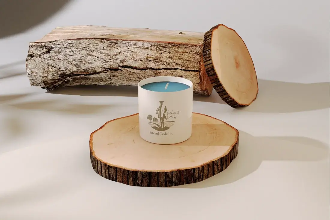 A Sentinel Candle Company candle on a wood slice beside a split log.