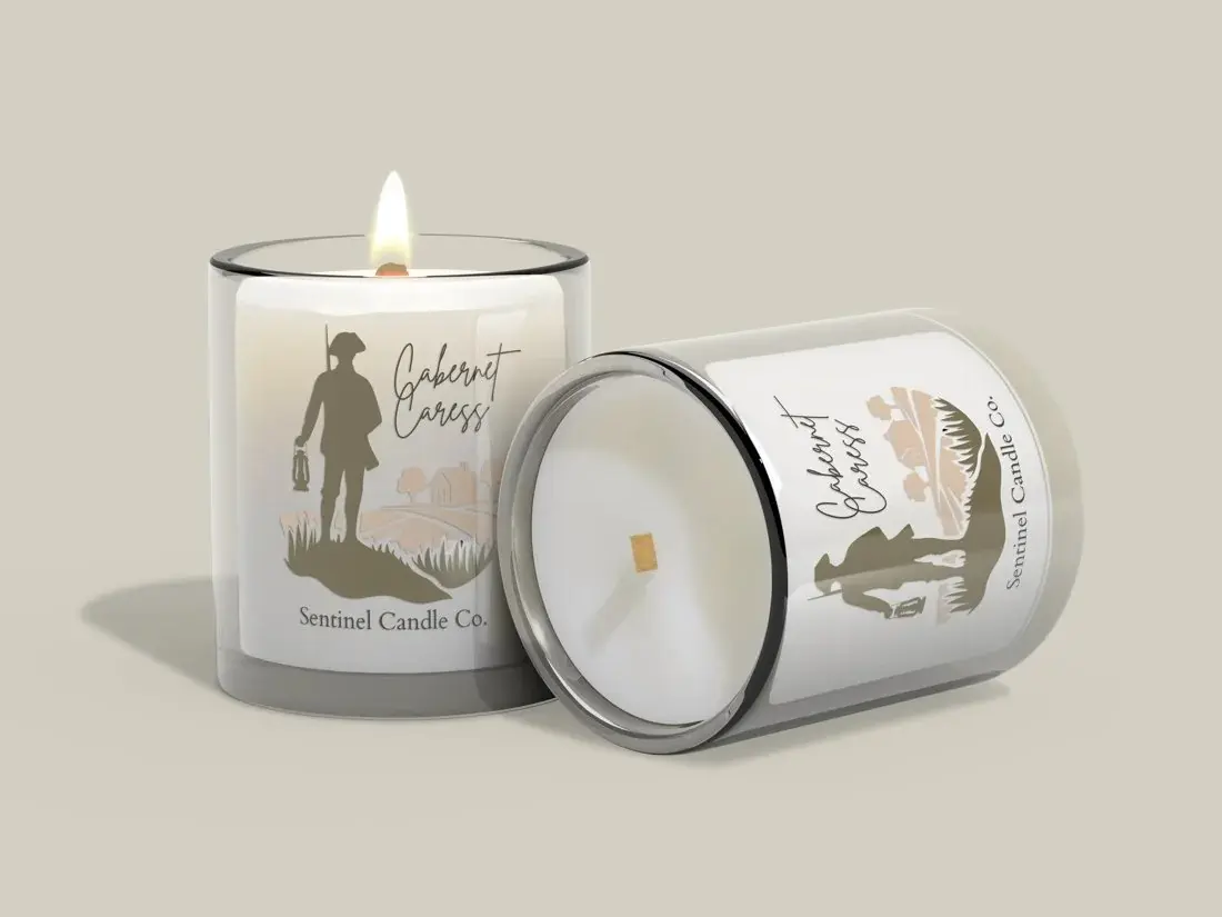 Two Sentinel Candle Company candles in glass jars, one lit, showing the illustrated lantern-carrying sentinel on the label.